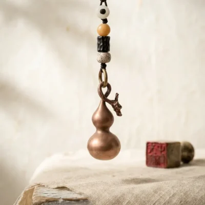 A solid Taoist copper gourd talisman with a dragon head design and bodhi seed beads, hanging above a rustic table