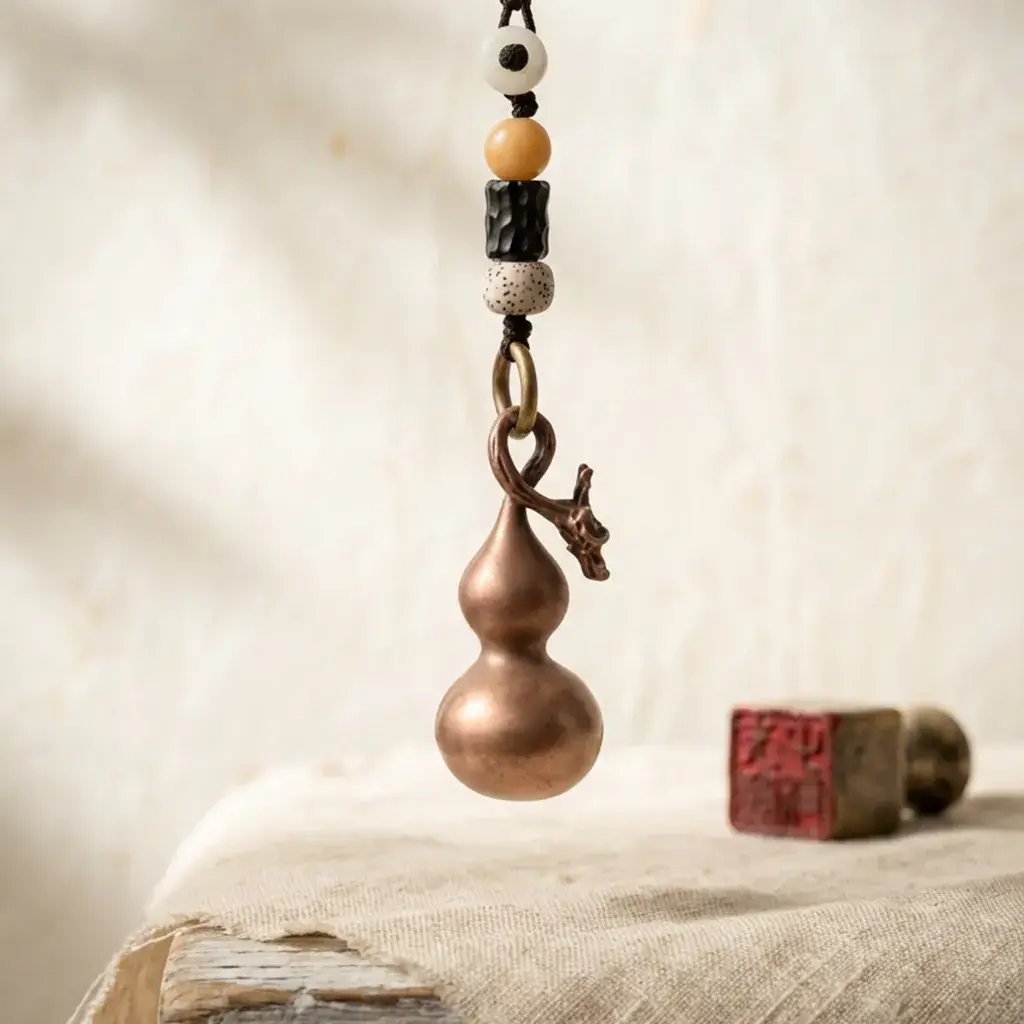 A solid Taoist copper gourd talisman with a dragon head design and bodhi seed beads, hanging above a rustic table